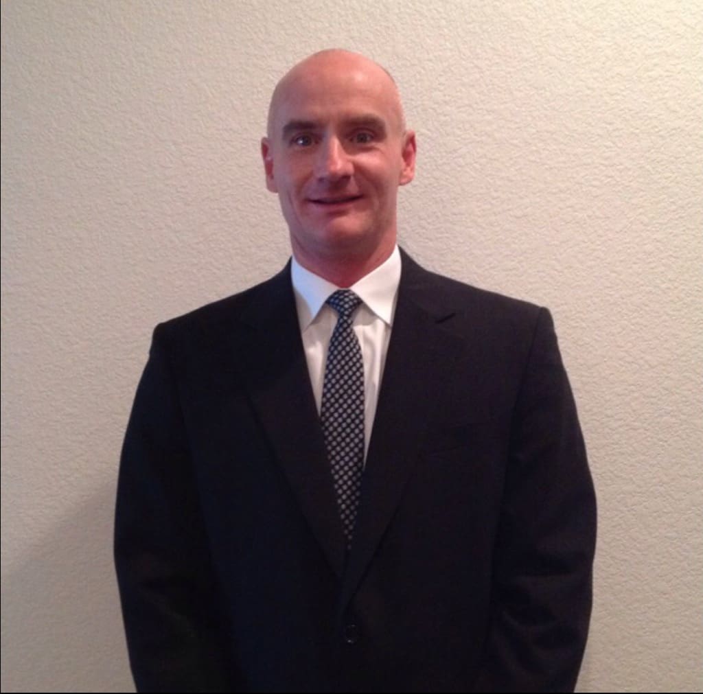 A man in a suit and tie standing next to a wall.