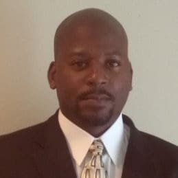 A man in a suit and tie standing up against a wall.