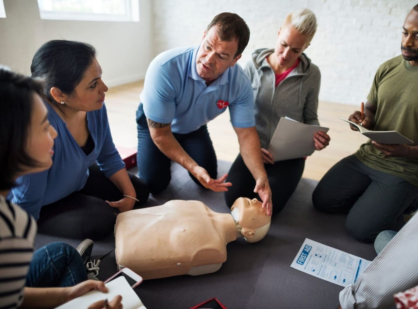 A group of people sitting around an instructor demonstrating cpr.