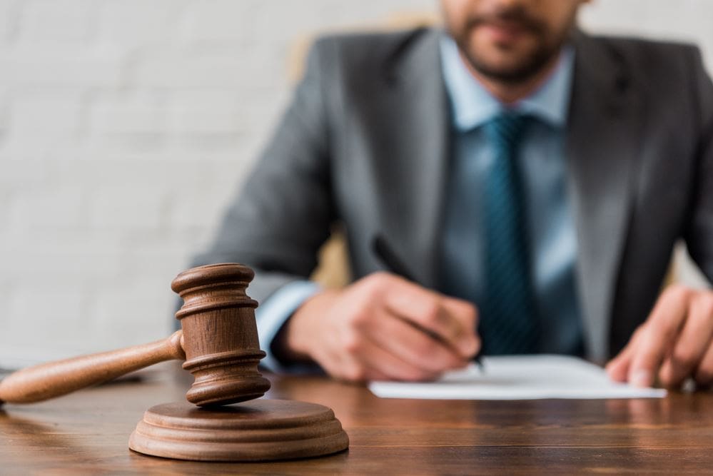 A man in suit and tie sitting at table with gavel.