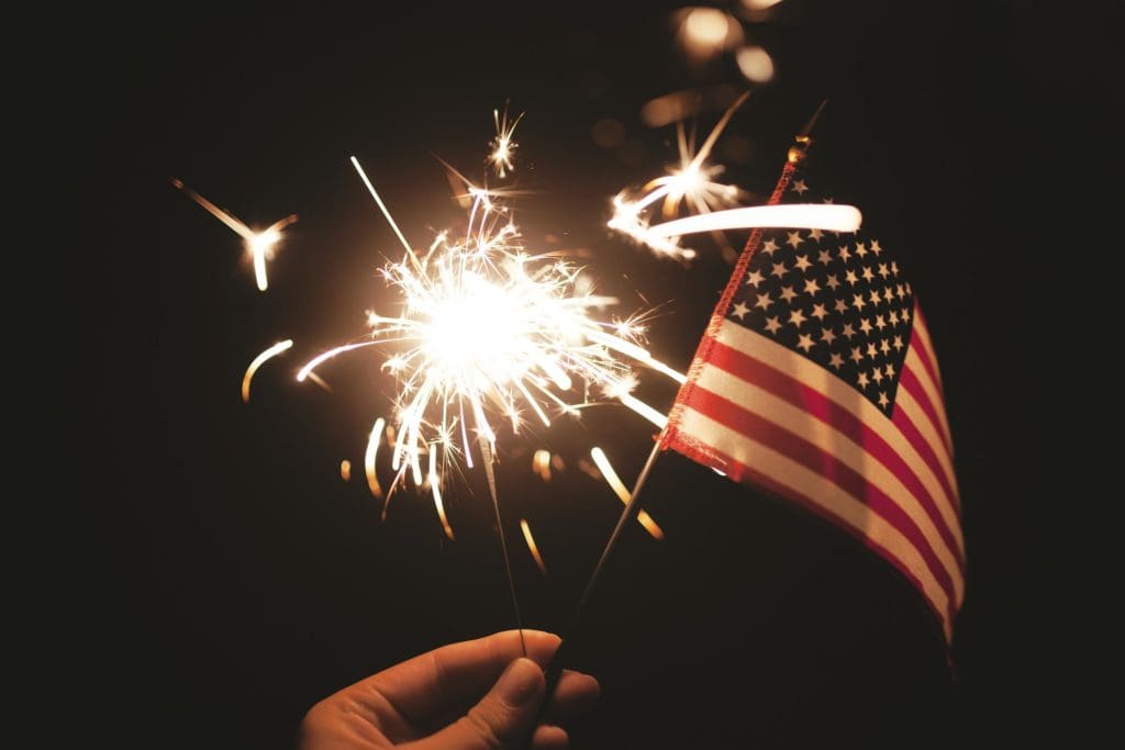 A person holding sparklers and an american flag.